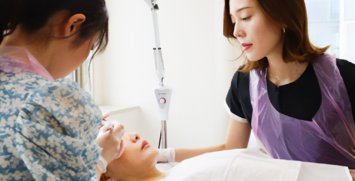 IMAAアートメイクスクールで講師の指導を受けて、人物の顔に医療アートメイク施術を行っている受講者。